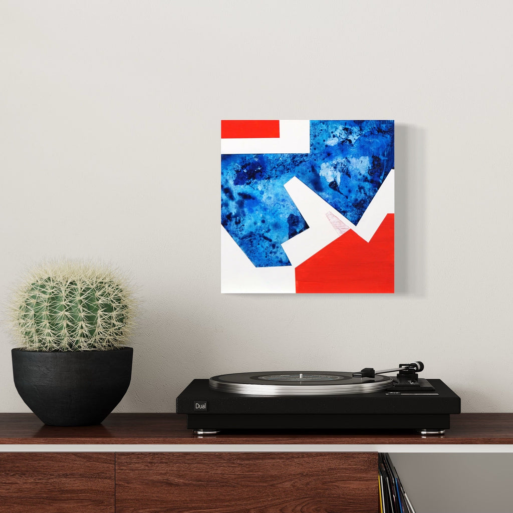 The artwork 'Red and Blue House' by Lisa Petker Mintz features a geometric abstract composition combining vibrant red and deep blue sections with crisp white angular shapes. The blue area showcases a marbled, watercolor-like texture while bold red segments create dynamic contrast. 12x12 inch acrylic painting on board captures modernist architectural elements.