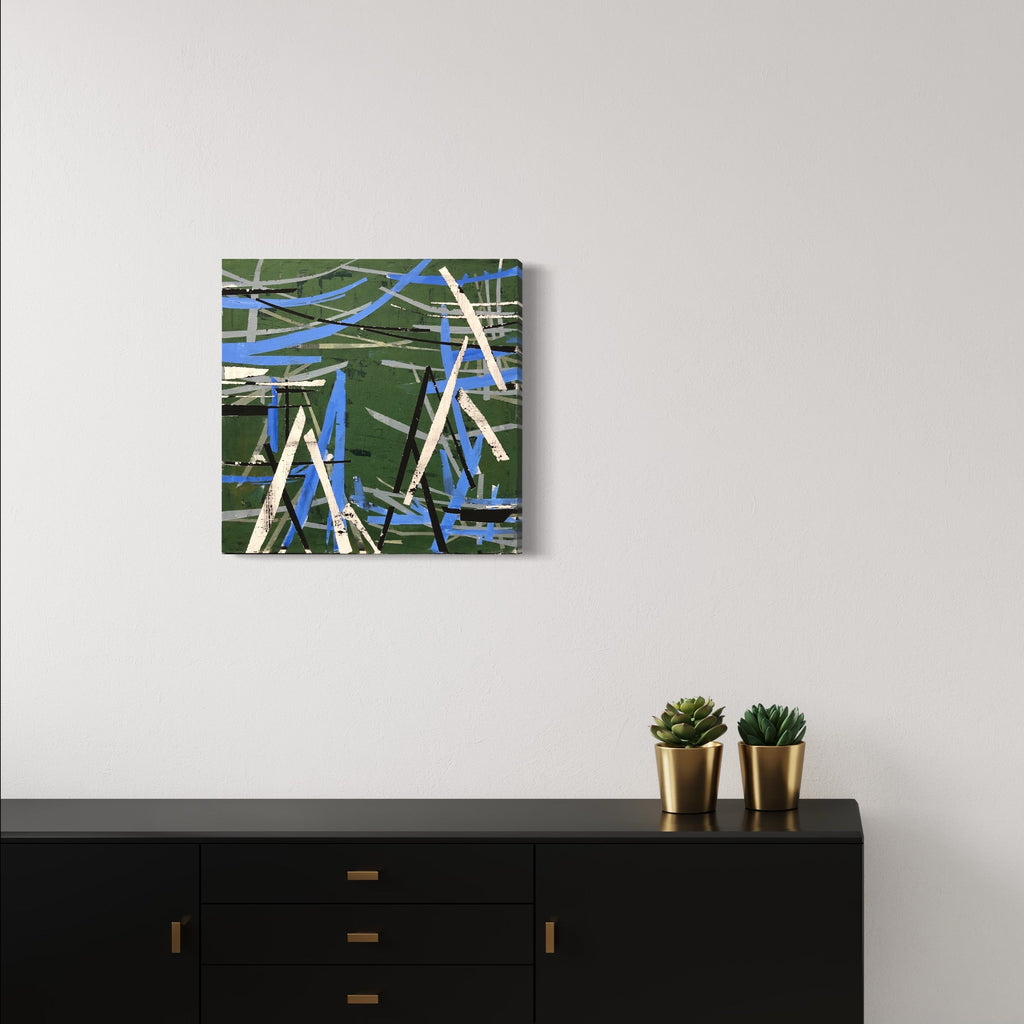The artwork 'Green Energy' by Shira Toren features dynamic intersecting lines in vibrant blue and forest green, created using Venetian Plaster on canvas. Abstract geometric patterns create a sense of movement and depth, with bold strokes layered to suggest industrial or mechanical elements. The 24x24 inch composition combines textural plaster techniques with a modern, energetic aesthetic.