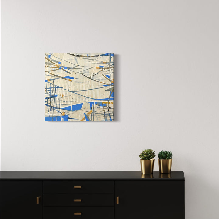 The artwork 'Curtain Call' by Shira Toren features dynamic intersecting lines in cool blue and neutral beige tones, created with Venetian plaster and pigment on canvas. Abstract geometric patterns create a sense of movement and depth, resembling fragmented curtains or shattered glass against a textured cream background. 26x26 inches abstract contemporary wall art by Shira Toren.