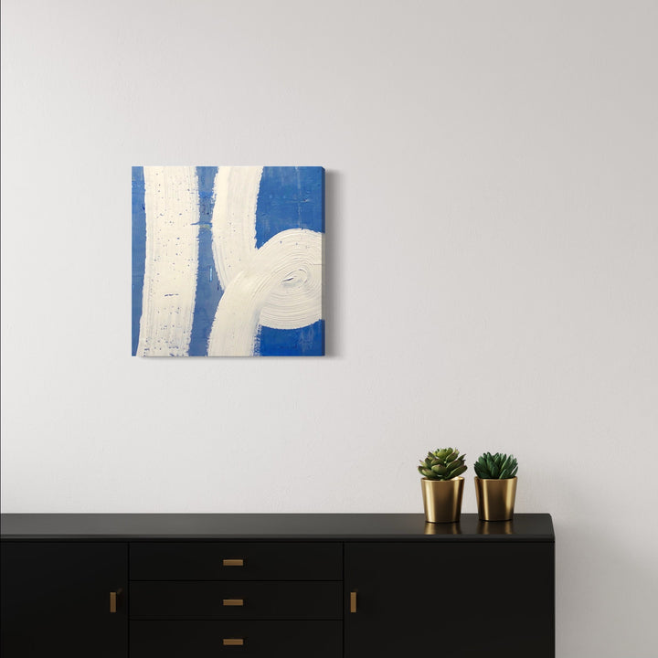 The artwork 'In the Loop' by Shira Toren features bold curved white lines against a vibrant cobalt blue background, created with Venetian Plaster and pigment on canvas. The abstract composition showcases sweeping geometric forms with a textured, dimensional surface, measuring 24 x 24 inches.