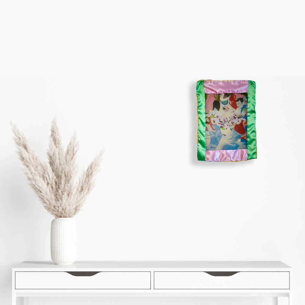 The artwork 'Orchid Eye Mini Quilt' by Eriko Hattori features abstract floral patterns layered with geometric shapes in pink, green, and brown tones. The quilt combines polyester georgette and satin fabrics with decorative grommets, creating a textured 12x15 inch wall piece with a modern artistic interpretation of orchids.