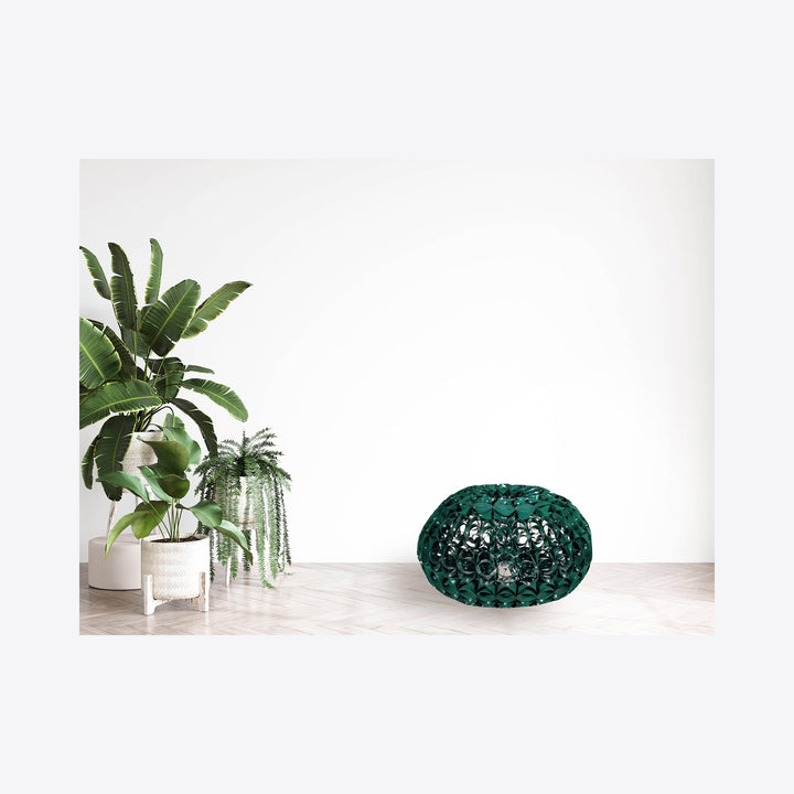The artwork 'Green Means Go' features a sculptural dome-shaped piece crafted from reclaimed aluminum with intricate riveted patterns, finished in deep emerald green. Displayed alongside verdant tropical plants in white planters, creating a minimalist modern composition against a clean white background. By Kate Rusek.