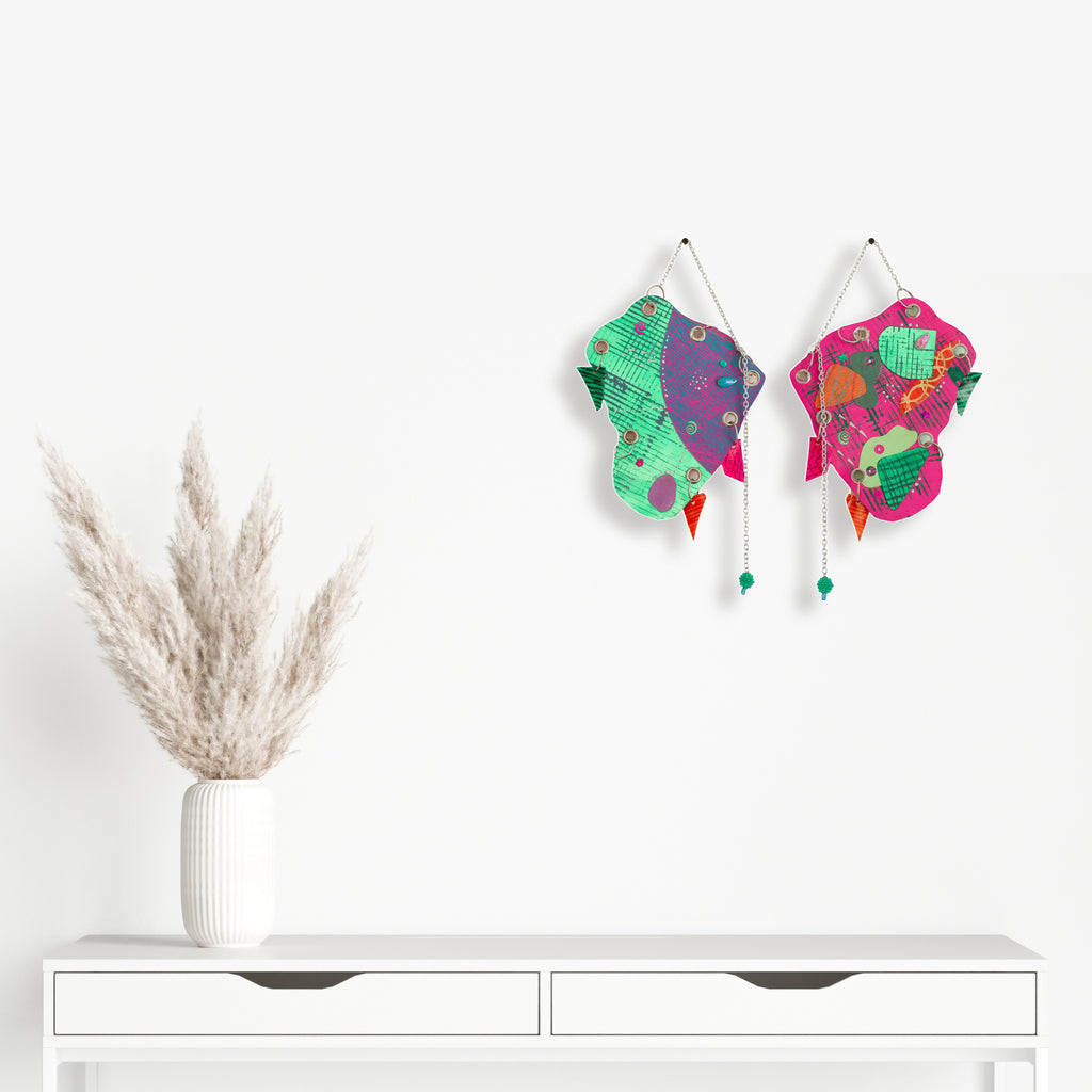 The artwork 'One Way Or Another' by Sunny Chapman features vibrant butterfly-shaped wall art with turquoise, pink, and purple patterns adorned with glitter, jewels, and metallic accents. Dangling beads and chains create elegant movement, while mixed media elements including sequins and handmade charms add dimensional texture and sparkle. By Sunny Chapman.