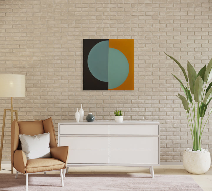 The artwork 'Rebirth' by Shyun Song features a minimalist geometric composition with a split circular form in muted teal blue against contrasting black and warm orange backgrounds. Oil on canvas abstract painting showcasing clean lines and color blocking, sized 30x30 inches, displayed above modern white furniture against textured brick wall.