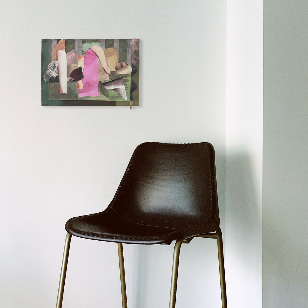 The artwork 'In The Stillness' by Winnie Sidharta features abstract watercolor composition with pink and gray geometric shapes layered against muted earth tones. The 12x18 inch piece showcases delicate painted cutouts and fluid watercolor techniques, creating a serene, contemporary aesthetic on paper. Wall art displayed above modern brown leather chair.