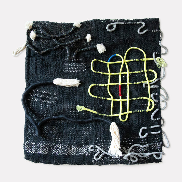 Intervened Couplets by Kathie Halfin: Abstract textile artwork featuring a black woven background with intricately stitched yellow geometric patterns, white thread accents, and silver curved elements. Made with flux yarn, nylon rope, cotton, and silver floss on a textured surface creating a contemporary mixed-media composition.