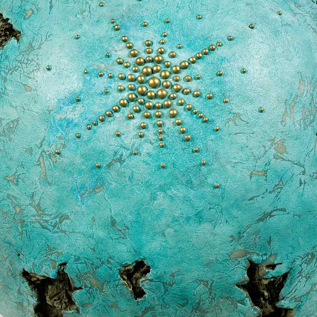The artwork 'IS' by Nora Chavooshian features a radiant starburst pattern created with bronze spherical elements arranged on a textured turquoise background. The metallic beads form an expanding circular design, contrasting beautifully against the weathered, aqua-colored forton surface with its organic textures and dark sculptural voids. Cast forton sculpture with bronze patina - by Nora Chavooshian.