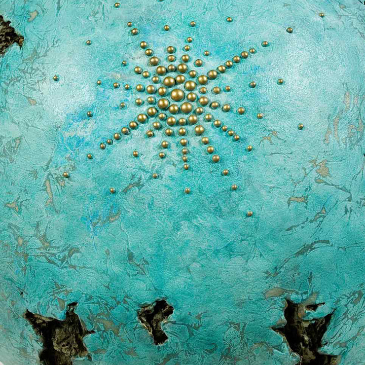 The artwork 'IS' by Nora Chavooshian features a radiant starburst pattern created with bronze spherical elements arranged on a textured turquoise background. The metallic beads form an expanding circular design, contrasting beautifully against the weathered, aqua-colored forton surface with its organic textures and dark sculptural voids. Cast forton sculpture with bronze patina - by Nora Chavooshian.