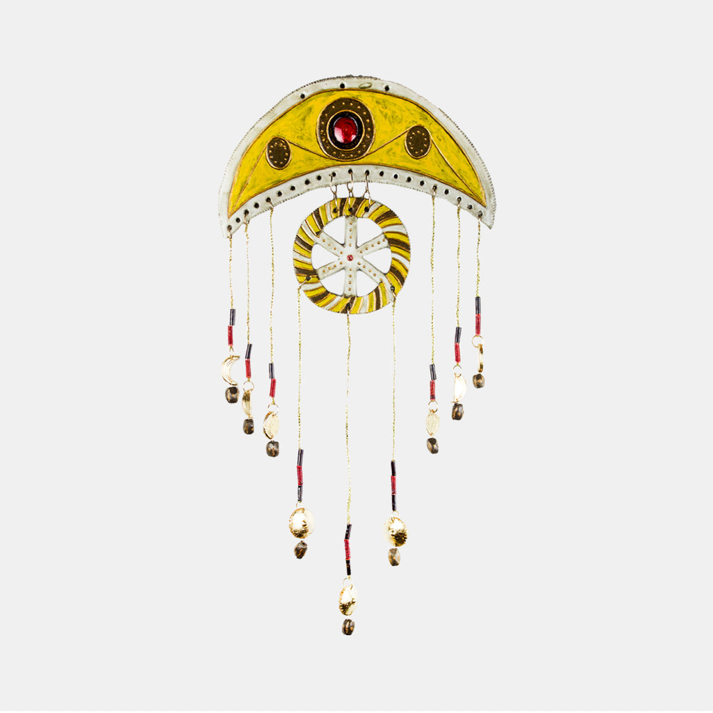 The artwork 'June' by Adina Andrus features a crescent-shaped ceramic wall piece with a vibrant yellow arc adorned with red gemstones. A central white spiral motif is suspended beneath, complemented by delicate hanging strands decorated with metallic beads and red accents. The 24k gold details shimmer against the glazed stoneware surface, creating an elegant dreamcatcher-inspired design.