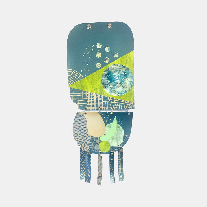 The artwork 'Juxtaposition' by Sunny Chapman features abstract geometric shapes in teal and lime green, with metallic grid patterns and circular elements. Mixed media collage combines monotype prints and textured paper, suspended by silver grommets. Layered composition creates depth through contrasting colors and patterns.