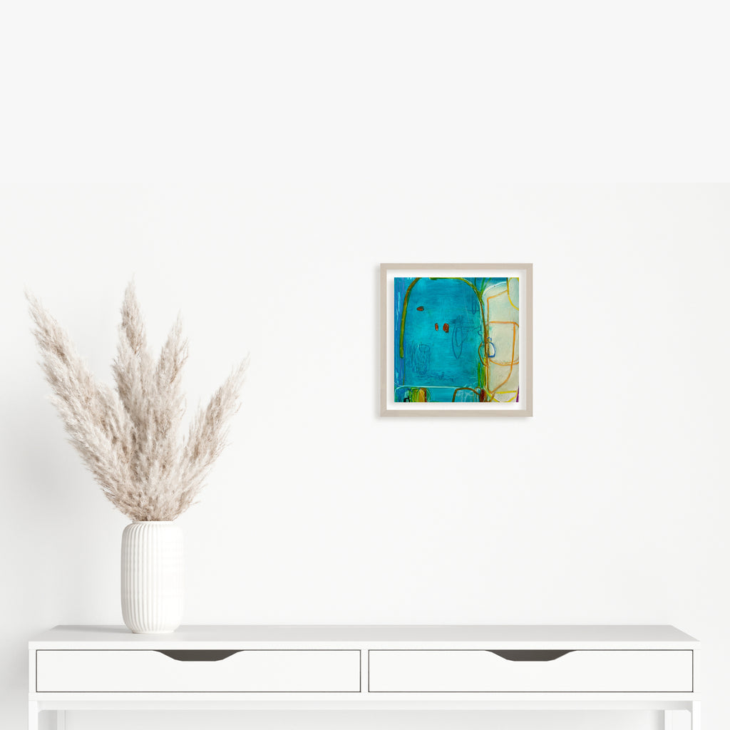 The artwork 'LS no. 20' by Janice La Motta features vibrant turquoise blue abstract forms blending with subtle yellow accents, creating a dynamic composition on Yupo paper. The oil pastel technique creates rich, textural elements against the smooth surface, displayed in a minimalist white frame. Original artwork measures 9x9 inches by Janice La Motta.