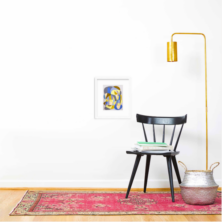 The artwork 'Lavender and Yellow on Lavender' by Alicia Little features an abstract composition in oil pastel and gouache, displaying flowing curves and organic shapes in soft lavender tones contrasted with vibrant yellow accents. The artwork is shown matted in a white frame, displayed in a minimalist interior setting with a black chair, brass floor lamp, and pink vintage rug - by Alicia Little