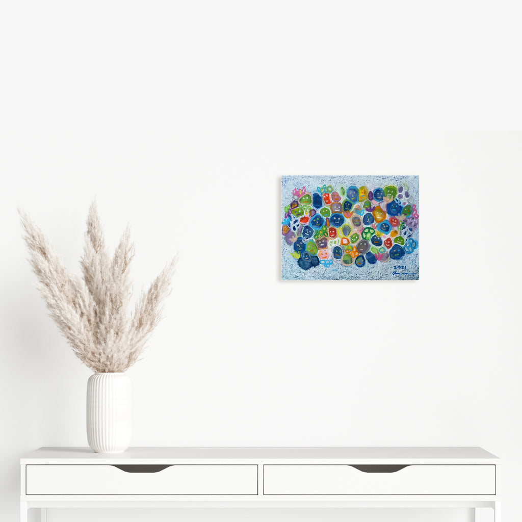 The artwork 'Living in a Community' by Ayane Kurai features vibrant circular patterns in blue, green, and multicolored dots scattered across a light blue watercolor background. The whimsical composition creates an abstract, bubble-like effect, expertly rendered in watercolor and cray-pas on paper, measuring 11 x 14.5 inches. By Ayane Kurai.