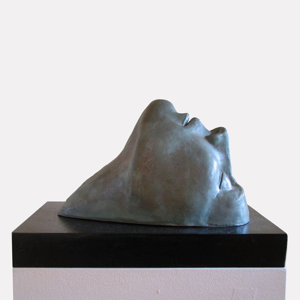 The artwork 'LUCKY' by Nora Chavooshian features a serene cast forton sculpture with a bronze patina, depicting an upward-tilted abstract form with flowing contours. The smooth, contemporary piece rests on a black pedestal, showcasing gentle curves and ridges that create a peaceful sculptural silhouette against a minimalist background.