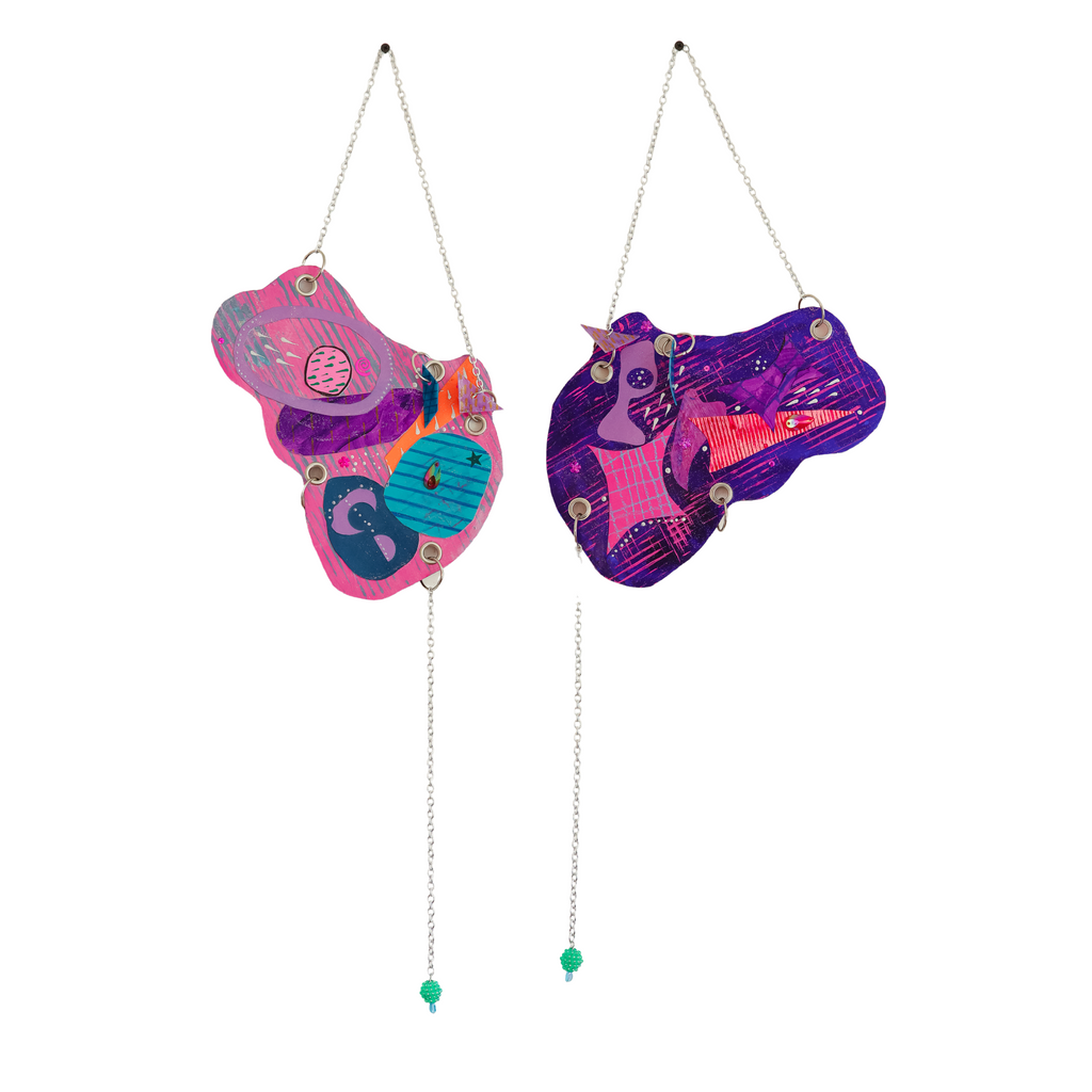 The artwork 'Lust For Sparkle' by Sunny Chapman features two abstract hanging shapes in vibrant pink, purple, and turquoise. Each shape is adorned with decorative elements including glitter, jewels, and metallic accents, connected by delicate silver chains with mint green beads. The mixed-media piece combines whimsical patterns and sparkly embellishments in a playful, symmetric composition. By Sunny Chapman.