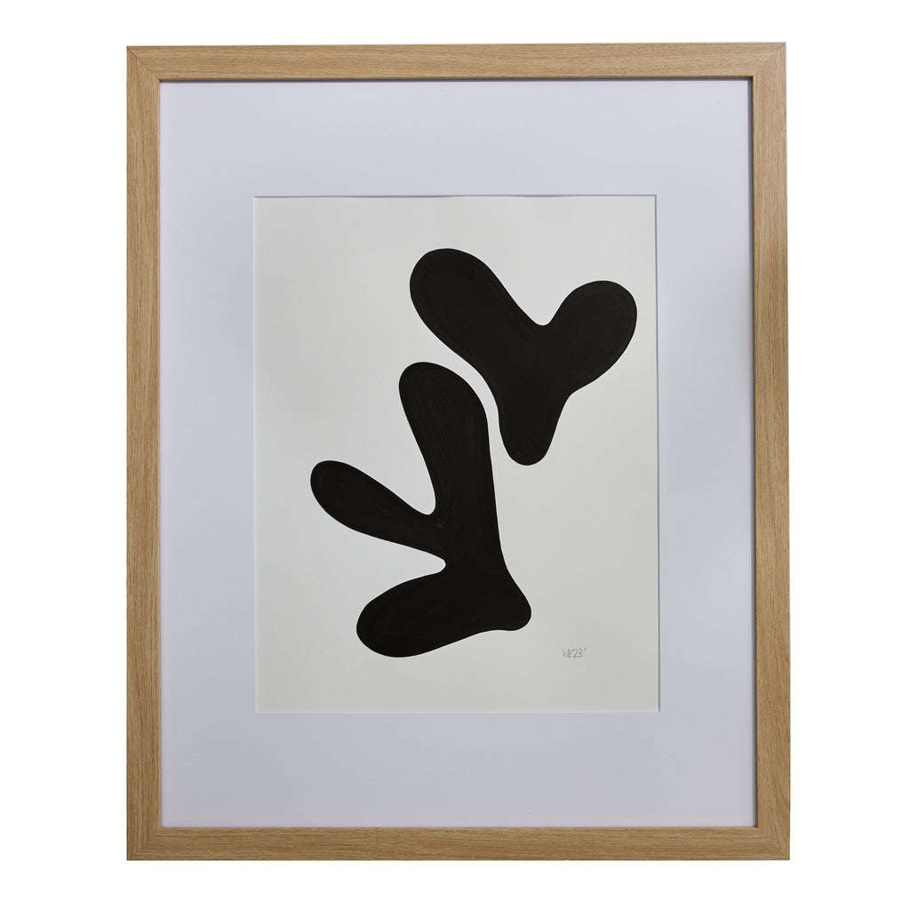 The artwork 'Morning Meditation XII' by Shadia Sabagh features bold black organic shapes on white paper, displaying abstract biomorphic forms reminiscent of growing plants or floating elements. The minimalist composition is executed in acrylic marker, professionally framed in light wood, creating a striking monochromatic contemporary piece.