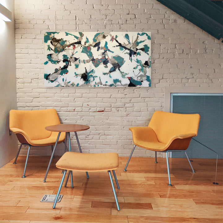 The artwork 'Making Honey' by Linda Lee Nicholas features abstract butterfly-like forms in vibrant teal and gray tones dancing across a white canvas. The acrylic on Dibond painting creates a dynamic composition with splashed and brushed elements, suggesting movement and organic flow. Displayed above modern orange chairs against a white brick wall. Created by Linda Lee Nicholas.