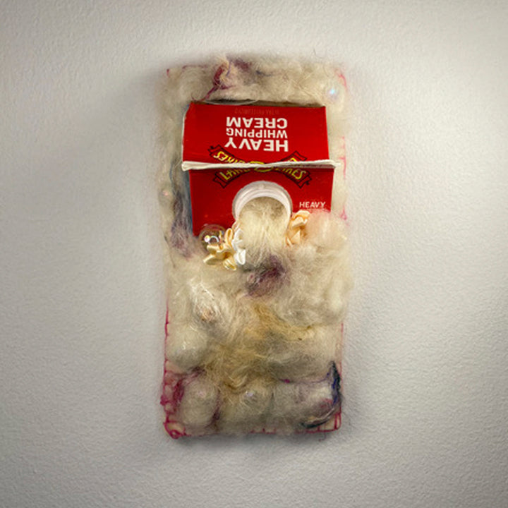 Miniature XIX by María Antonia Villaseñor-Marchal: A mixed-media sculpture featuring a repurposed red cream carton adorned with delicate wool, alpaca, and silk fibers in ethereal whites and subtle pink hues. Glass and acrylic beads add sparkle while satin ribbon provides elegant detail. The textural composition creates a soft, cloud-like appearance.