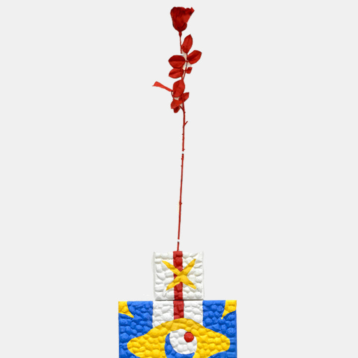 The artwork 'Neither Here Nor There A' by Marco DaSilva features a striking red floral stem emerging from a textured geometric base composed of white, yellow, and blue segments. The base displays a quilted, bubble-like texture with rhinestone accents, while the vibrant red painted flower stem rises gracefully against a stark white background.