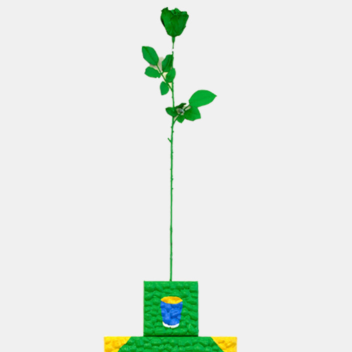 The artwork 'Neither Here Nor There E' by Marco DaSilva features a vibrant green rose stem emerging from a geometric base of layered squares in green and yellow. The stem bears glossy leaves and a stylized flower, embellished with rhinestones against a white background. Latex paint and polyurethane create a luminous finish, with a small blue accent in the center block.