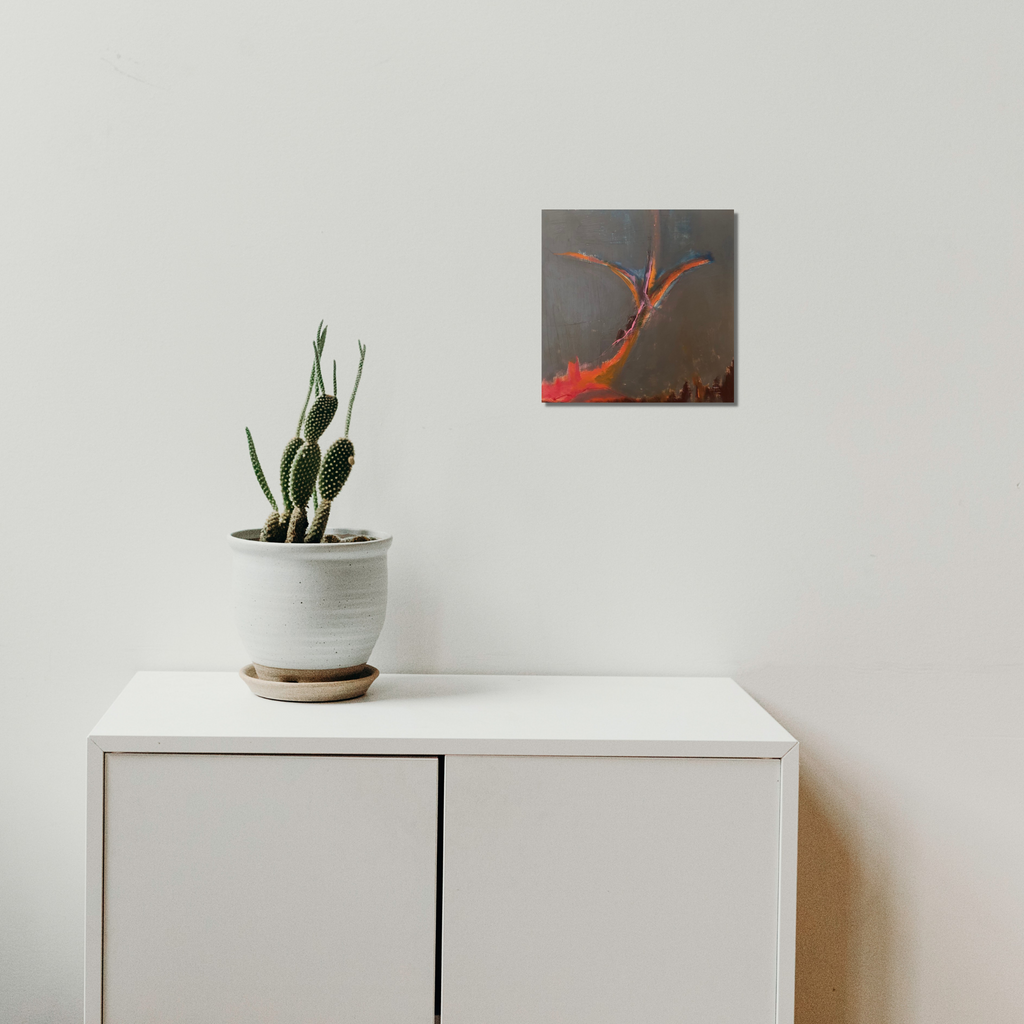 The artwork 'Orange Sapling' by Beth Barry features vibrant orange gestural brushstrokes against a deep charcoal background, creating an abstract organic form that appears to branch upward. The 12x12 inch acrylic painting on panel captures dynamic movement and natural growth patterns, complementing the minimalist white interior setting.