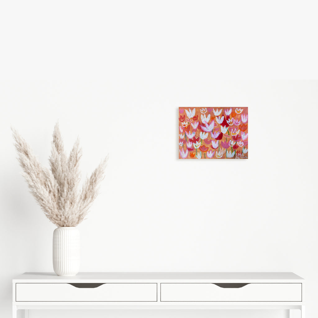 The artwork 'Orange Tulip' by Ayane Kurai features a vibrant pattern of stylized tulips in various shades of orange, pink, and white against a warm coral background. Created with watercolor and cray-pas on paper, the 9x12 inch piece showcases a whimsical, repetitive floral design with delicate brush strokes and soft pastel textures.