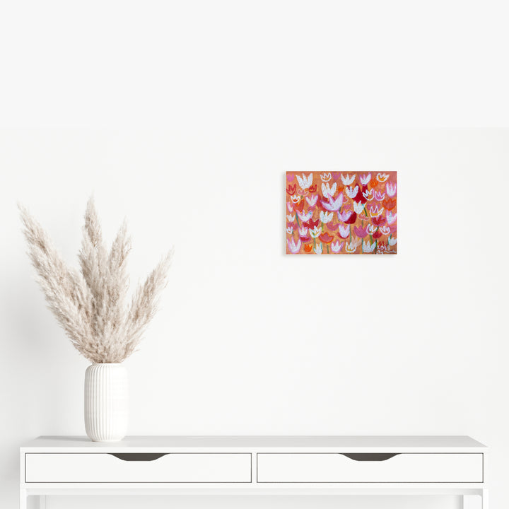 The artwork 'Orange Tulip' by Ayane Kurai features a vibrant pattern of stylized tulips in various shades of orange, pink, and white against a warm coral background. Created with watercolor and cray-pas on paper, the 9x12 inch piece showcases a whimsical, repetitive floral design with delicate brush strokes and soft pastel textures.