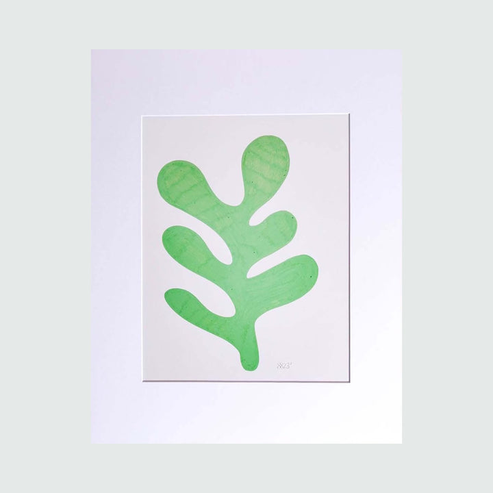 The Morning Meditation Series 4 by Shadia Sabagh features a minimalist freehand drawing of a bright green organic leaf shape, reminiscent of a Matisse-inspired cutout, set against a crisp white background. The botanical form shows gentle curves and rounded lobes, creating a serene and contemplative limited edition print.