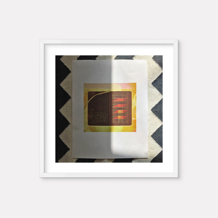 The artwork 'October 16 2015' by Anne Sherwood Pundyk features a minimalist digital print composition with a central gold-toned square containing red linear elements and handwritten text against a dark background. The piece is presented in a white frame against a geometric black and white chevron pattern surface.