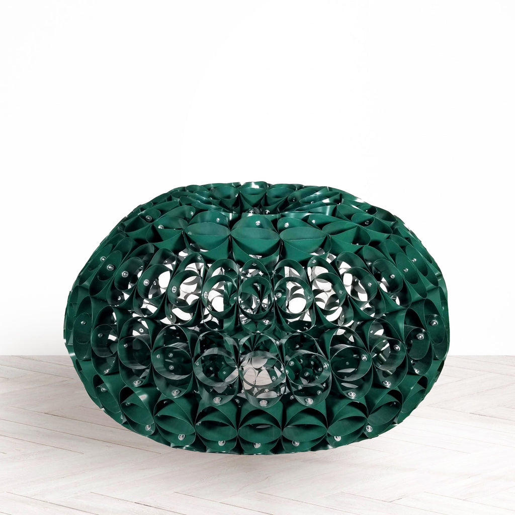 The artwork 'Green Means Go' by Kate Rusek features an intricate spherical sculpture crafted from reclaimed aluminum. The emerald-green metallic surface displays a mesmerizing honeycomb pattern with riveted connections, creating a complex latticed structure. The piece exhibits a harmonious blend of industrial materials and organic forms, with light filtering through the geometric openings.