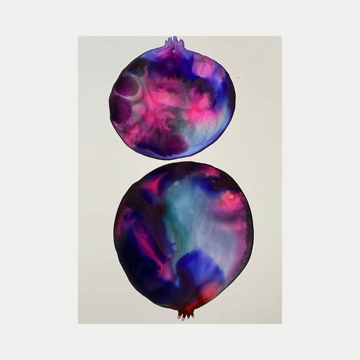 The artwork 'Pink Pomegranate' by Arielle Stein features two abstract pomegranate shapes rendered in vibrant watercolor-like ink. The fruits display swirling patterns of deep purple, electric pink, and ethereal blue tones, creating a cosmic, dreamy effect on white paper. The organic forms show fluid color transitions and translucent layering techniques.