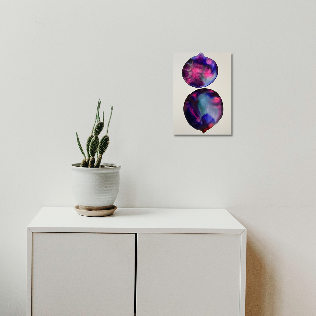 Pink Pomegranate by Arielle Stein: Abstract ink artwork featuring two circular shapes in vibrant pink, purple, and blue watercolor-like effects. The organic spherical forms create a dreamy, cosmic appearance on white paper. Modern minimalist wall art displayed above white cabinet with potted cactus.