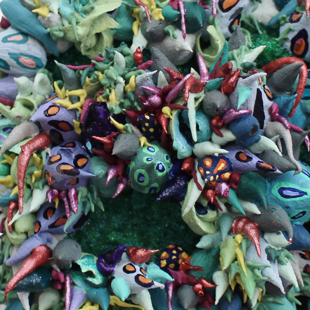 The artwork 'Plexaurella' by Seren Morey features an intricate circular arrangement of coral-like forms in vibrant turquoise, purple, and mint green, adorned with metallic coral-pink accents. Glass beads and ultralight acrylic create a textured, reef-inspired pattern with organic shapes and flowing tentacle-like elements, showcasing a dynamic underwater aesthetic.