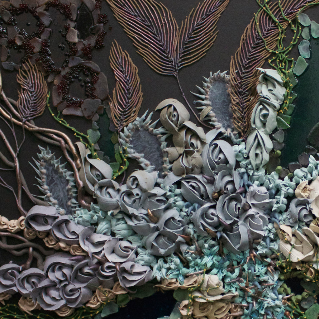 The artwork 'Primordial Arabesque' by Seren Morey features intricate layered patterns resembling underwater coral formations, with delicate feather-like fronds in bronze tones against a dark background. Swirling, textured elements in pale blue-grey and seafoam green create organic shapes, enhanced by glass beads and beach glass that catch light. The mixed media piece combines acrylic and urethane to achieve a dimensional, marine-inspired effect.