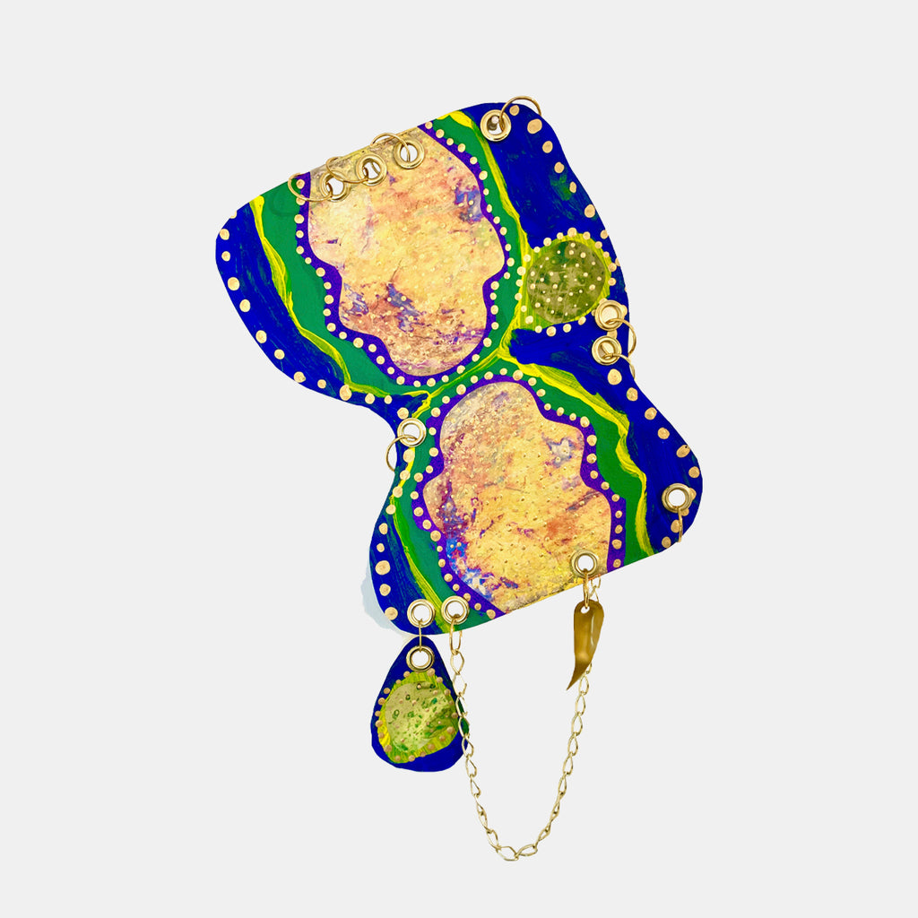 The artwork 'Remembrance 1' by Sunny Chapman features an abstract composition with fluid organic shapes in vibrant royal blue and emerald green borders. Golden-peach central forms are adorned with dotted white accents and purple highlights. A small chartreuse pendant element hangs from a delicate chain, creating a jewelry-like aesthetic in acrylic on paper.