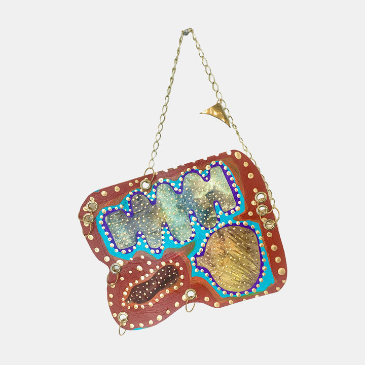 The artwork 'Remembrance 6' by Sunny Chapman features abstract organic shapes on reddish-brown background, decorated with dotted borders and vibrant blue outlines. The mixed-media piece incorporates metallic gold accents and shimmering textures, suspended by a delicate gold chain. Acrylic on paper, 12x14 inches, showcasing a contemporary folk art style with intricate detail work.