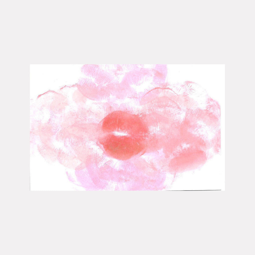 The artwork 'Flower Kiss' by Ronit Levin Delgado features a vibrant lipstick print in coral red, surrounded by delicate pink watercolor-like impressions creating a dreamy, floral effect on white paper. The central kiss mark appears to float amid soft, cloud-like rose-tinted shapes, merging artistic expression with feminine sensuality.