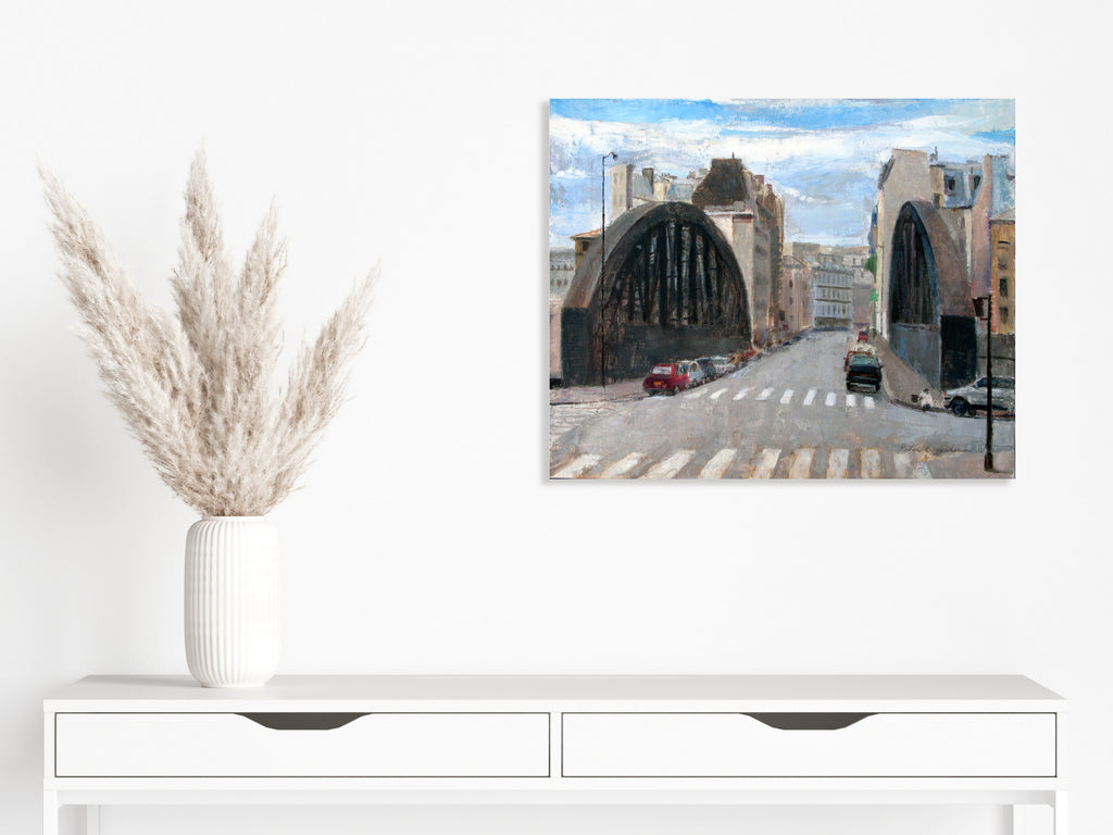 The artwork 'Rue Aqueduc' by Peter Colquhoun depicts an urban street scene with two dramatic arched bridges spanning across the road. Oil on linen captures the soft blue sky, industrial architecture, and city buildings in muted tones. Parked cars line the street, with distinctive crosswalk stripes in the foreground, creating a realistic Montreal cityscape.