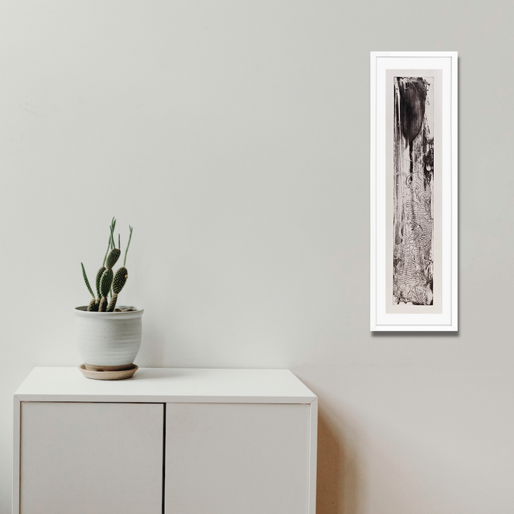 The artwork 'Sea Shadow' by Barbara Groh features a vertical monochromatic etching with dramatic black ink strokes cascading down a textured surface, creating an abstract representation of flowing water. The piece combines bold gestural marks with subtle tonal variations, displayed in a crisp white frame, measuring 31 inches in height and 7 inches in width.