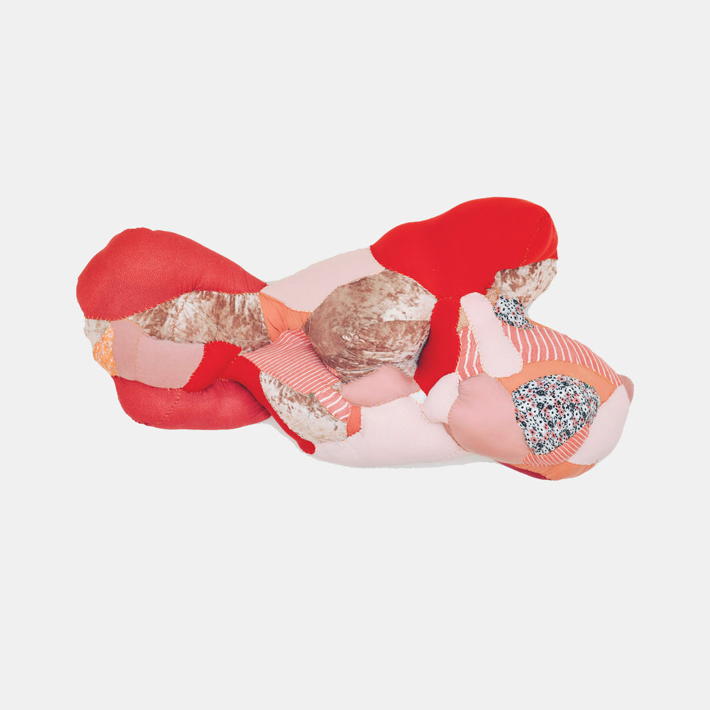 The artwork 'Semi-supine' by Hanna Washburn features an abstract textile sculpture combining red, coral, and blush pink forms. Made from recycled clothing and textiles, the piece creates organic, flowing shapes with varied textures including smooth, quilted, and sparkled patches, mounted on a wood panel backdrop. The composition suggests a reclining form conveyed through soft, undulating curves.