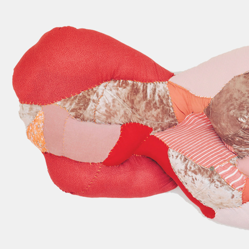 The artwork 'Semi-supine' by Hanna Washburn features an abstract textile sculpture combining vibrant red and coral tones with soft pink hues. The piece presents a flowing, organic form created from layered recycled clothing and textiles, with textural striped patterns and quilted elements mounted on wood panel. The composition suggests a reclining or wavelike movement.