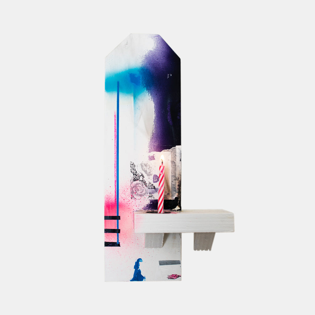 The artwork 'Shrine to the Letter' by Troy Medinis features a vertical white shrine-like structure with ethereal spray paint gradients in turquoise, purple, and pink. A miniature birthday candle and decorative transferred imagery rest on a minimalist shelf, creating a contemplative mixed-media composition using gesso, molding paste, and spray paint techniques. By Troy Medinis.