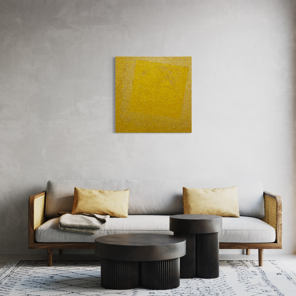 The artwork 'Hommage to MK' by Valerie Hallier features a vibrant yellow square canvas adorned with delicate flower petals, displayed above a modern sofa with cane sides and white cushions. Two black cylindrical coffee tables and a geometric patterned rug complete the contemporary living space setting. 30x30 inches, mixed media on canvas by Valerie Hallier.