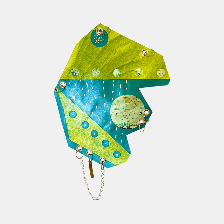 The artwork 'Space Shower' features a geometric composition with vibrant lime green and turquoise sections, depicting abstract rainfall patterns with white brushstrokes against a teal background. Metallic chain details and circular elements suggest celestial bodies, creating a playful cosmic bathroom scene. Acrylic on paper, 16x12 inches by Sunny Chapman.