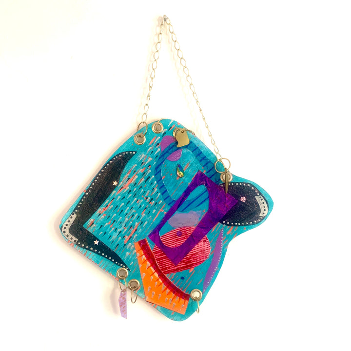 The artwork 'Spate' by Sunny Chapman features vibrant abstract shapes on a 12x12 inch paper. The composition showcases dynamic forms in turquoise, purple, and orange acrylic paint, with distinctive brush strokes creating a flowing pattern. The piece hangs from a delicate gold chain, combining contemporary artistic expression with modern display elements. Art by Sunny Chapman.