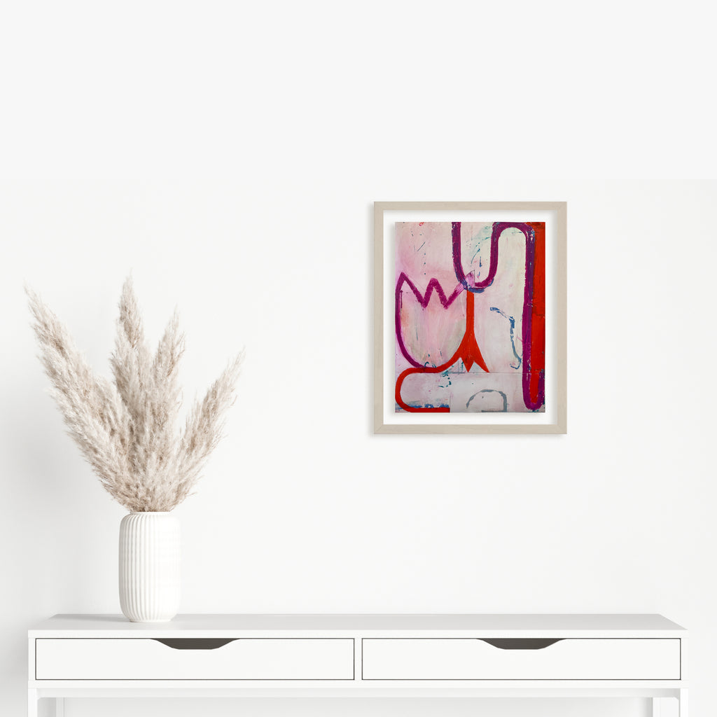 Spring Fling 6 by Janice La Motta: Abstract oil pastel artwork featuring fluid organic shapes in pink, red, and blue tones against a light background. Bold curved lines create a playful, dynamic composition on Yupo paper, with gestural marks suggesting natural forms and movement. Framed in white, displayed above modern white furniture.