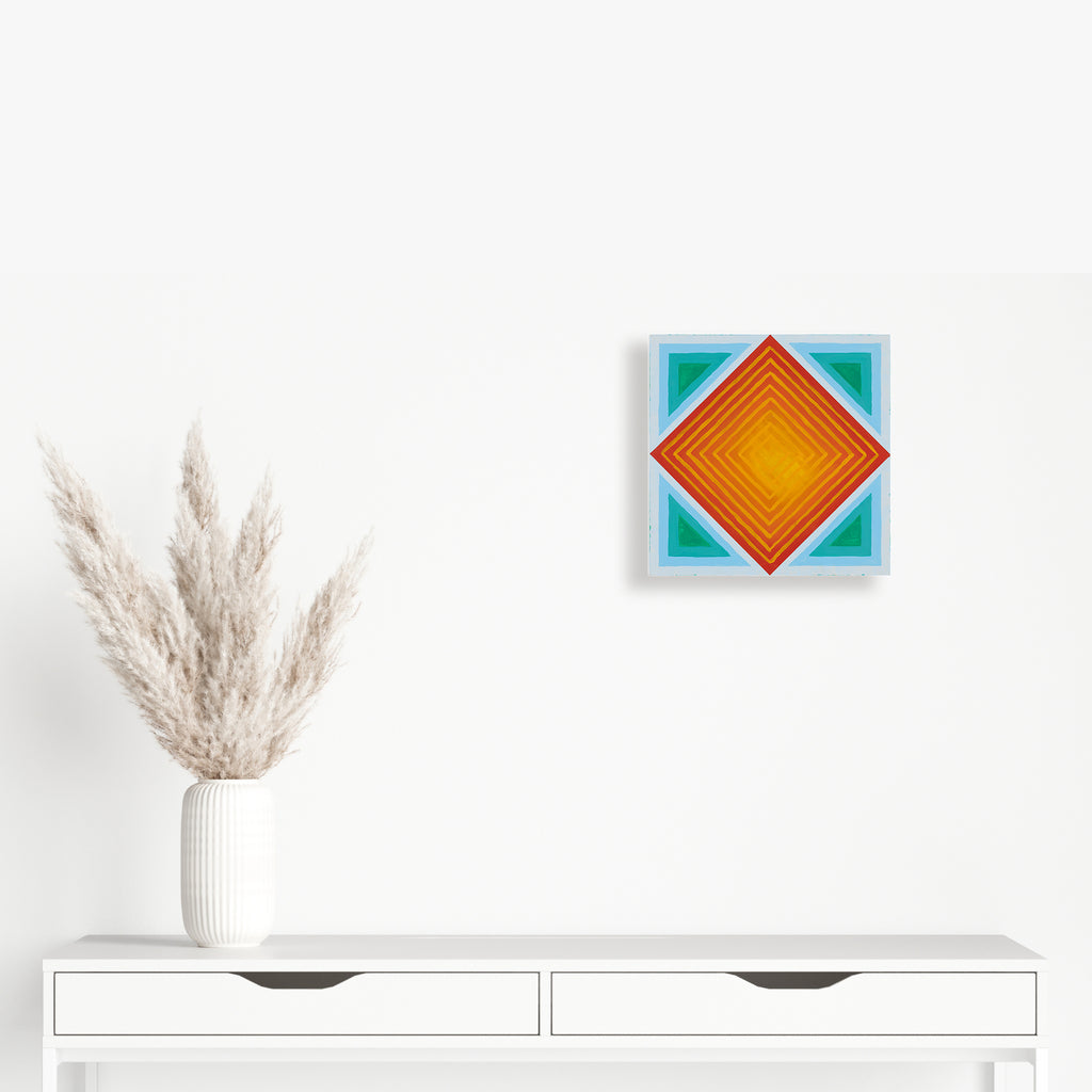 The artwork 'Square Loop' by Amber Heaton features a striking geometric composition with concentric diamond shapes in vibrant orange and yellow tones, nested within a turquoise square frame. The 12x12 inch acrylic painting on panel creates a mesmerizing optical illusion through precise linear progression, showcasing modern minimalist design with bold color contrast.
