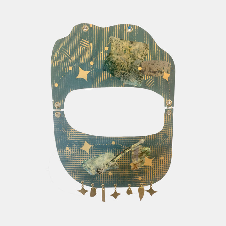 The artwork 'Starscape' by Sunny Chapman features an abstract oval-shaped frame in teal and gold with geometric patterns, metallic stars, and textured collage elements. A central window opening is surrounded by delicate linear details and hanging star charms, creating a celestial mixed-media composition on metallic paper with grommets. - By Sunny Chapman