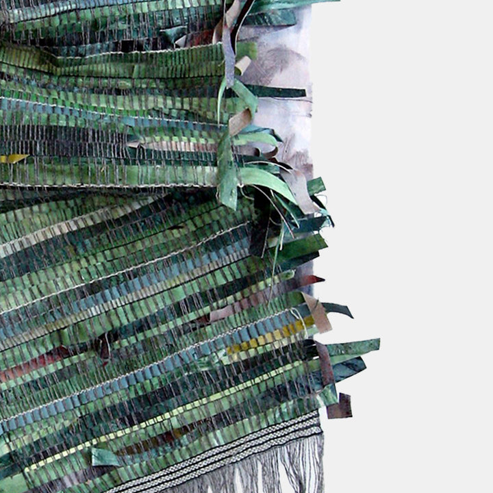 The artwork 'Stripes Earned' by Christina Massey features intricate layered strips of green and teal textiles, creating a dynamic vertical composition. Woven yarn elements cascade downward, while textural variations in the acrylic-painted canvas and linen strips create depth and movement. The piece combines mixed media techniques with a forest-inspired color palette.