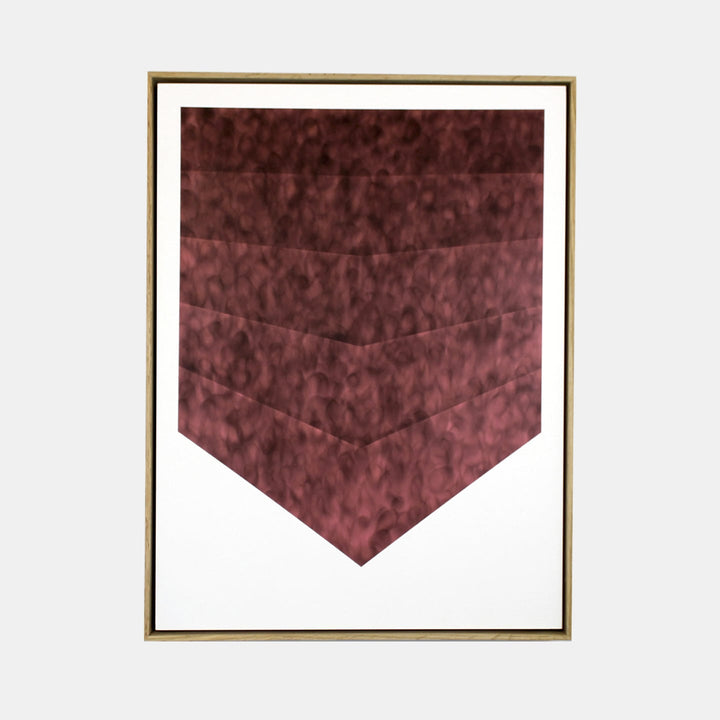 The artwork 'Sunlight In The House' by Evan Ishmael features a geometric chevron pattern in deep burgundy tones created with soot and spray-applied acrylic. The textured layers descend in a V-shaped formation against a stark white background, framed in elegant gold trim, showcasing a modern minimalist aesthetic at 24x18 inches.